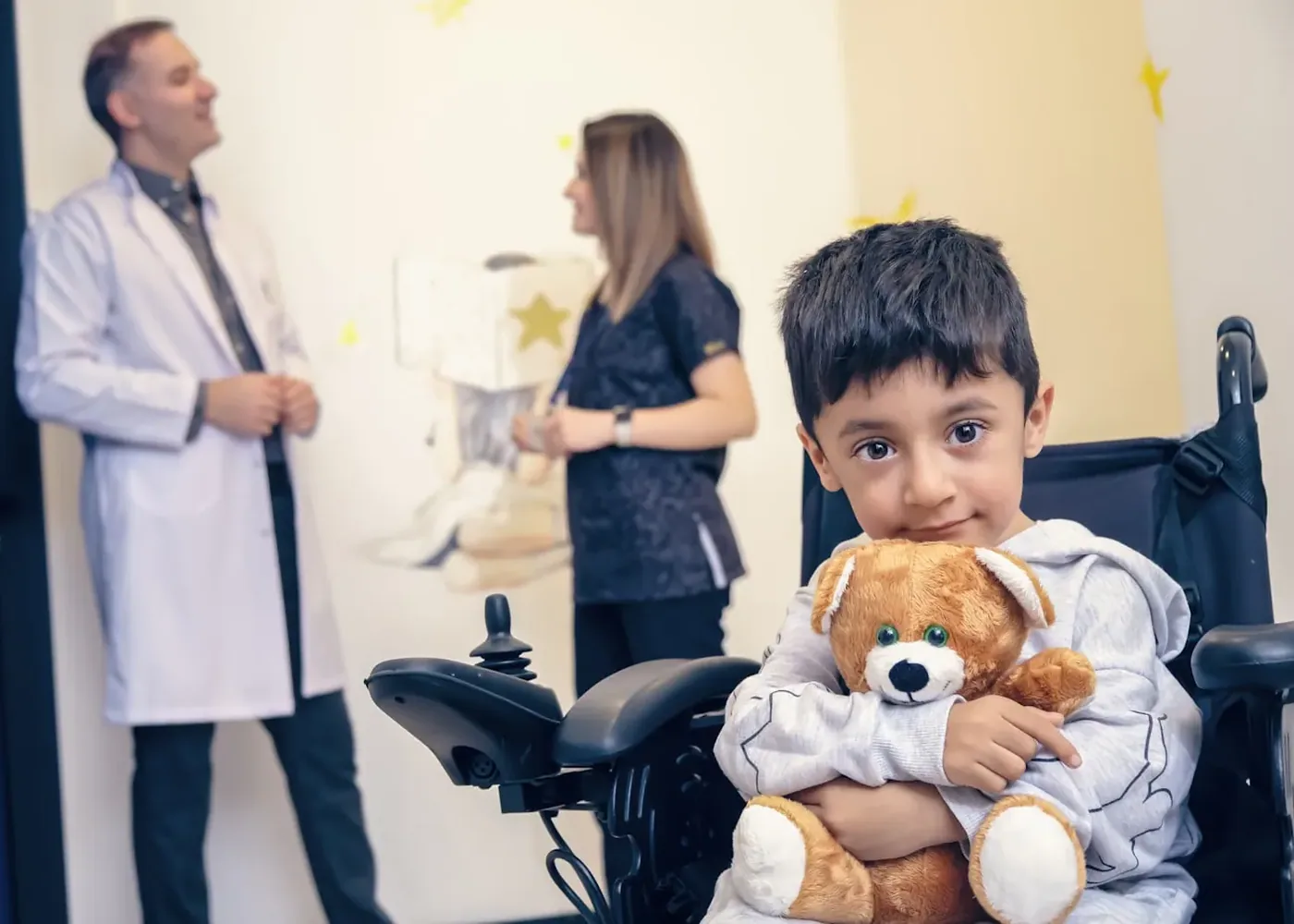 A child in a wheelchair with a clinician and a parent.